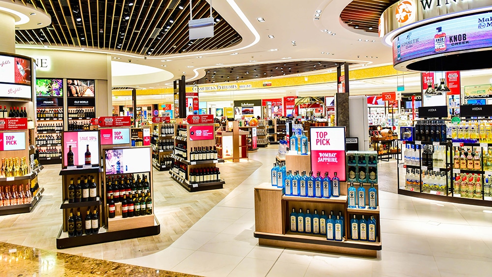 Interior de tienda en Barcelona, dentro del aeropuerto, donde se ven múltiples expositores de retail, con perfumes, cosméticos y botellas de alcohol.
